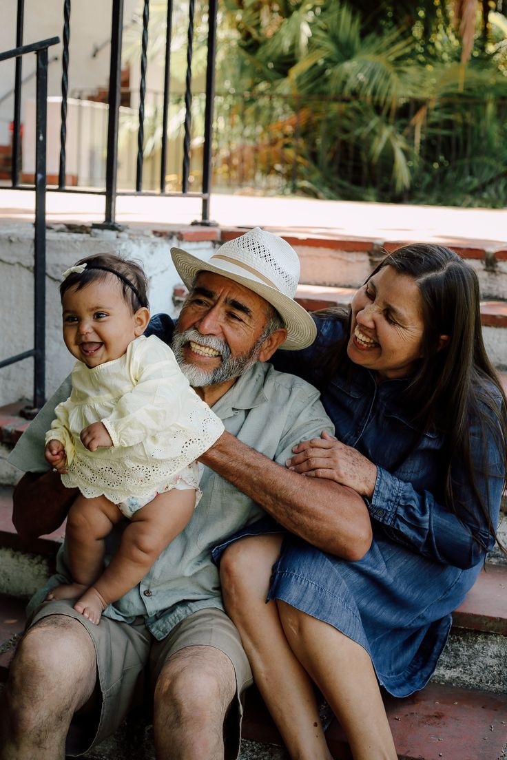 Grandparents sitting outdoors with their baby granddaughter, laughing together — warm, loving family moment