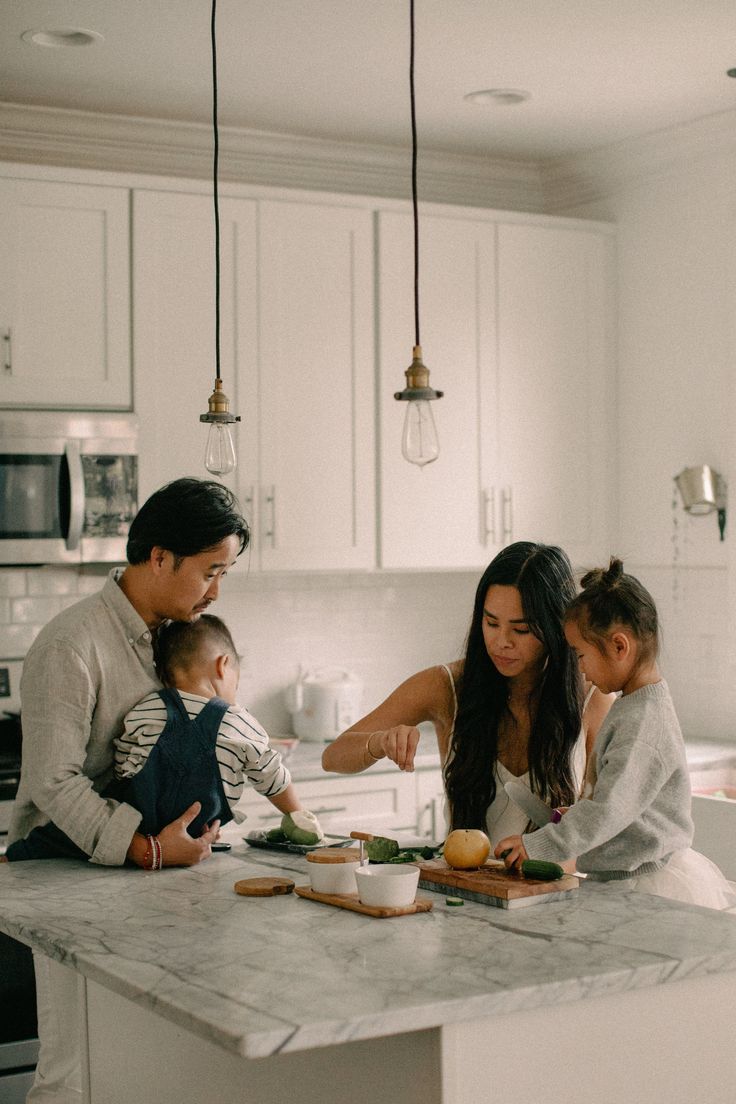 Asian family preparing food together in the kitchen — father holding baby, mother and daughter cooking, warm and natural home moment