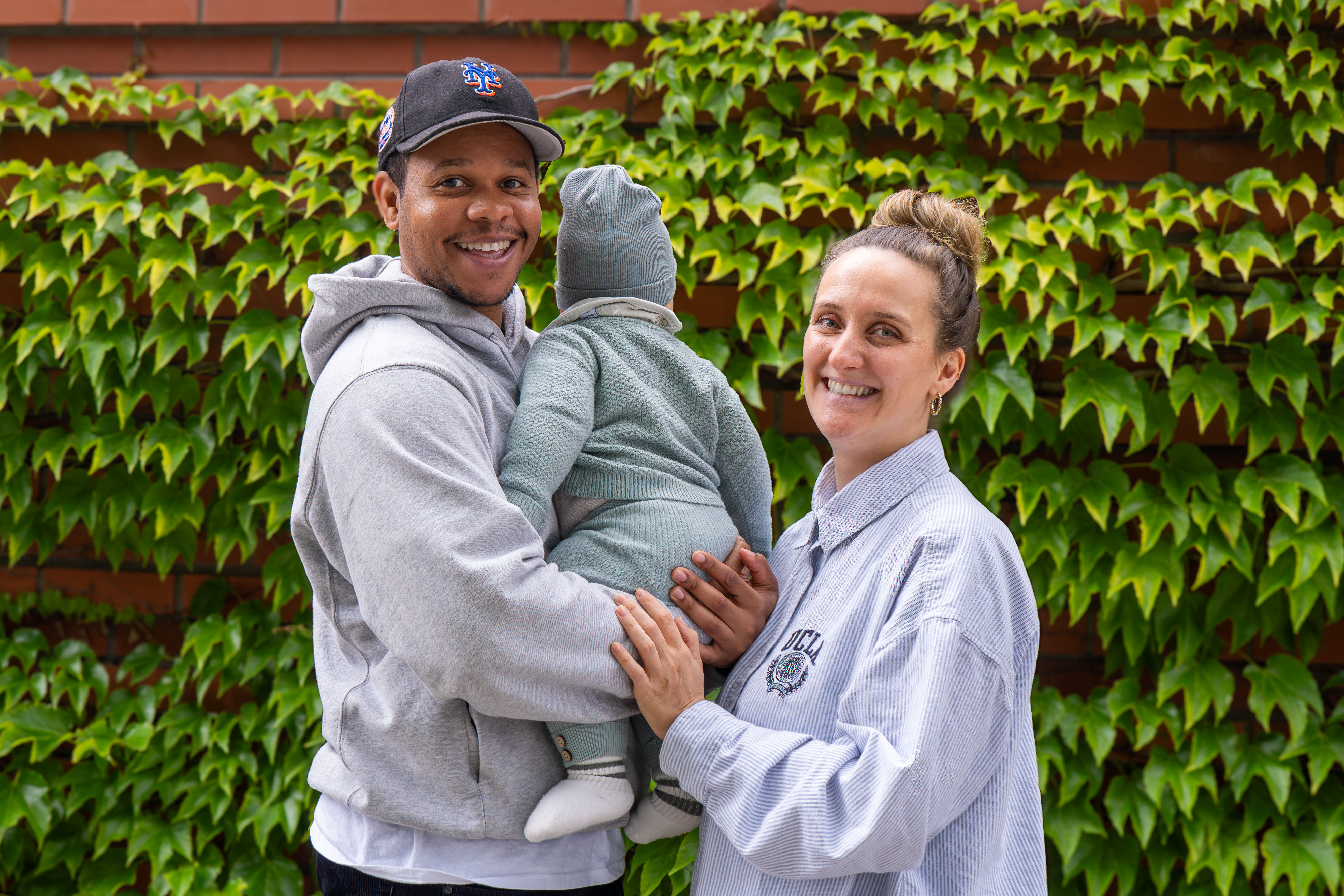 Alexander and his partner holding their son outdoors in front of an ivy-covered brick wall — the family behind ThyroKid